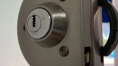 מנעול דלת ממד עם צילינדר ממתכת, ממוקם בזווית על דלת מזכוכית.